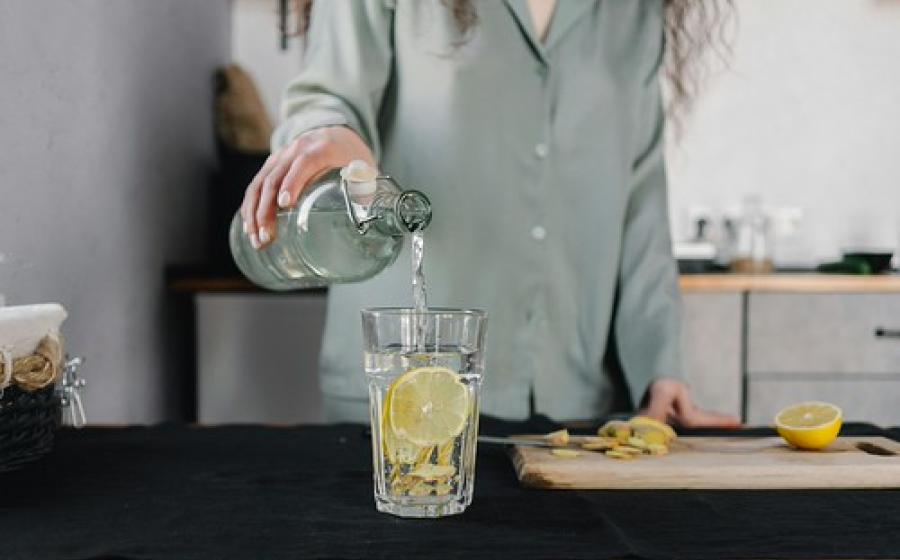 Woman standing behind a counter pouring water into a clear glass with a lemon slice in it