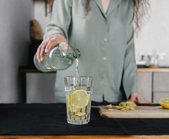 Woman standing behind a counter pouring water into a clear glass with a lemon slice in it